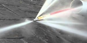 Close-up of a high-pressure spray nozzle cleaning a dark textured surface.